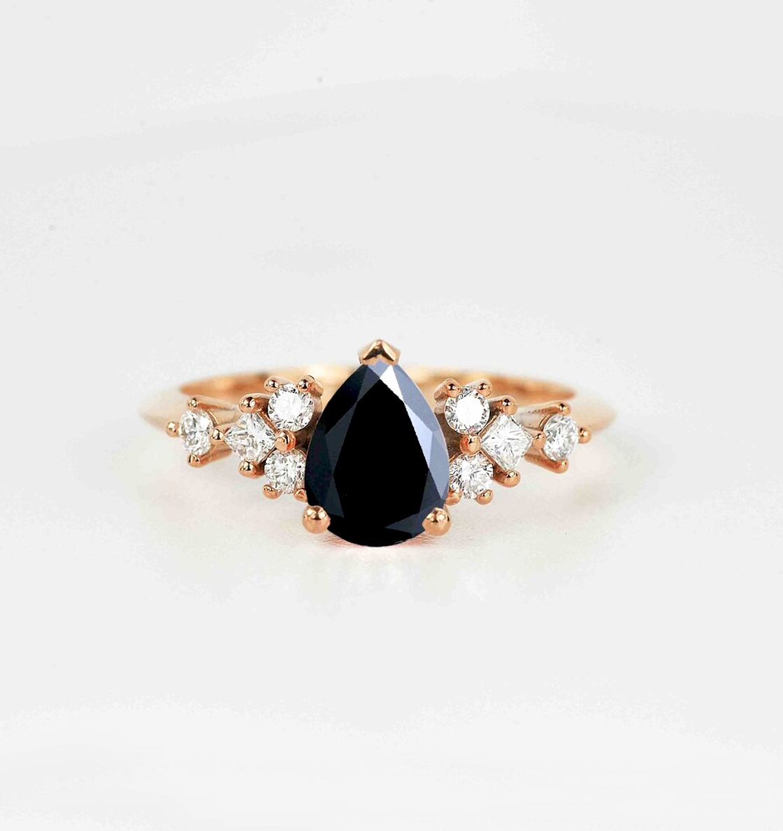 A natural pear cut black diamond and princess, round cut diamond cluster ring in solid rose gold.